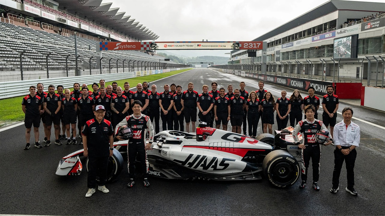 Haas-teammedlemmer og japanske gæster poserer med en Formula 1-bil på Fuji Speedway