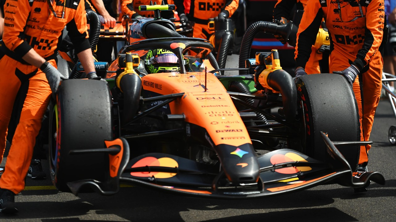 McLaren mekanikerleri, pit alanında turuncu bir Formula 1 aracının etrafında çalışıyor.