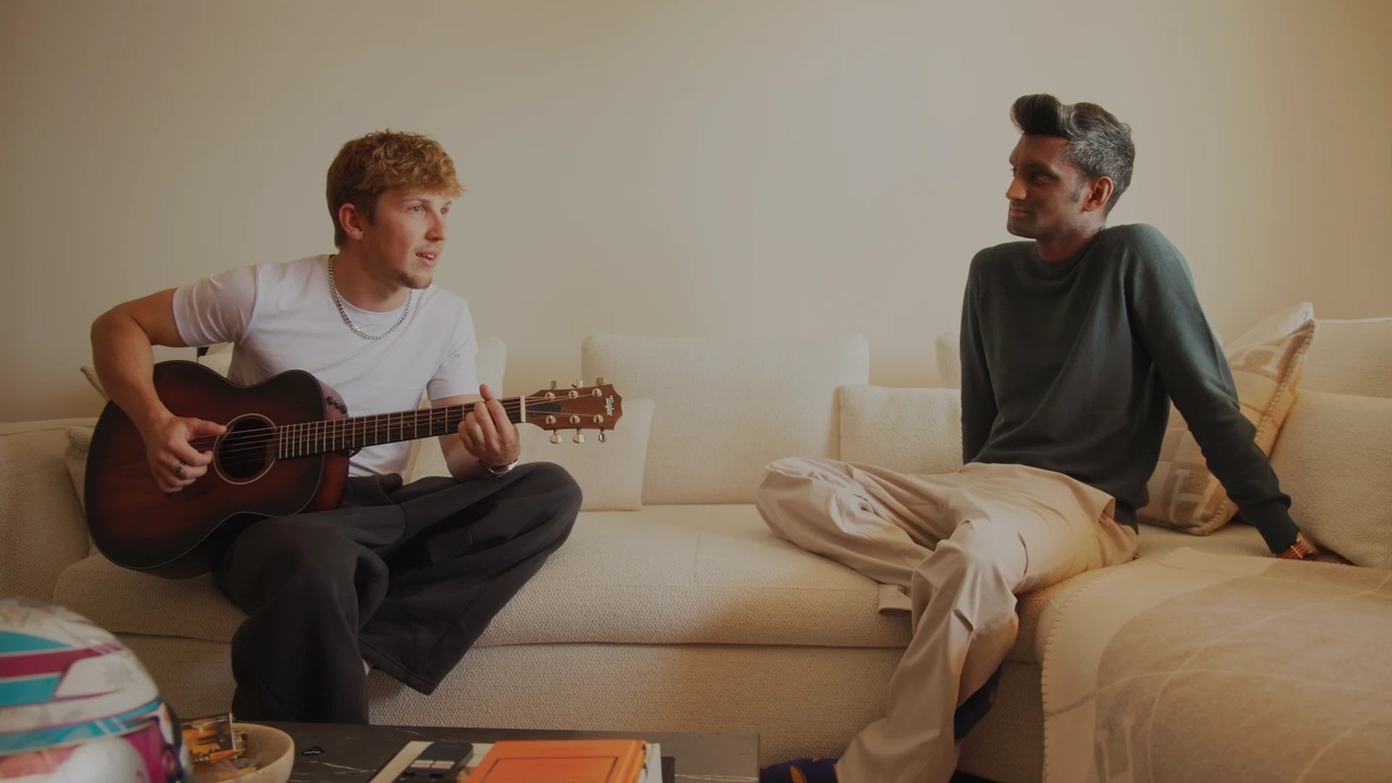 Liam Lawson hält eine Gitarre, während er neben einem anderen Mann sitzt